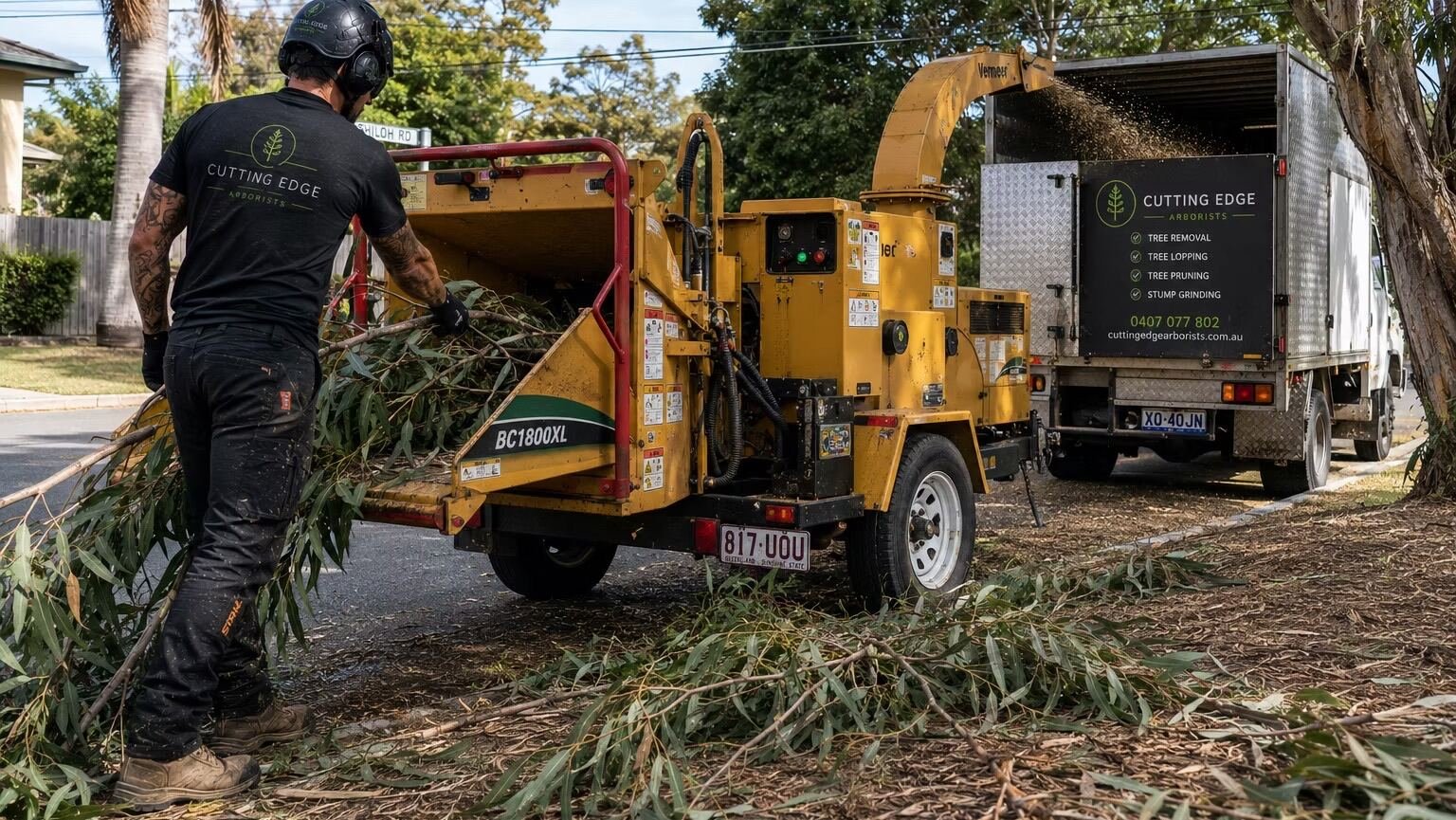 Cutting Edge Arborists crew feeding branches into a wood chipper beside their branded truck